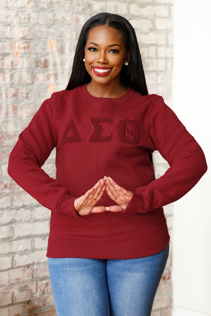 A woman wearing a Crimson sweatshirt with the letters  ΔΣΘ. Solid ΔΣΘ Chenille Sweatshirt, snugger fit if desired.