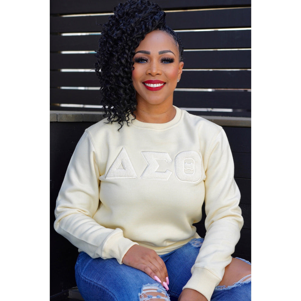 A woman wearing a Cream sweatshirt with the letters  ΔΣΘ. Solid ΔΣΘ Chenille Sweatshirt, snugger fit if desired.